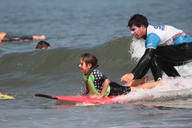 The instructor helps his student to surf the wave 